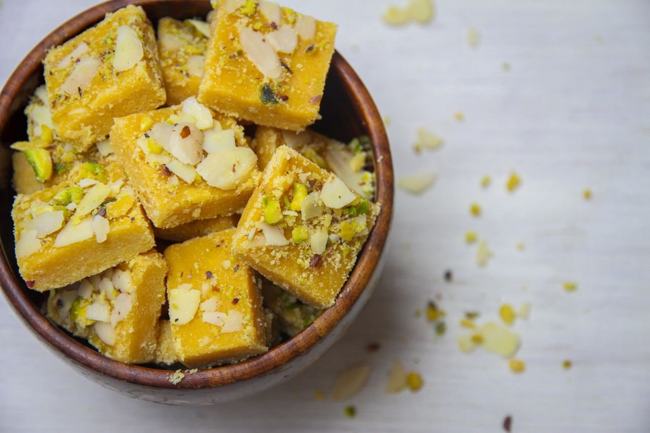 Top view of delicious Indian besan barfi garnished with almonds and pistachios, served in a wooden bowl.